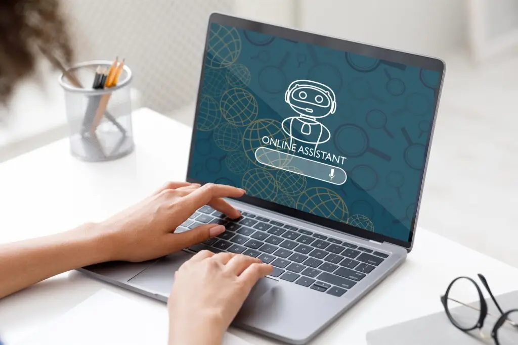 Hände tippen am Laptop, auf dem Bildschirm ein KI-Assistent